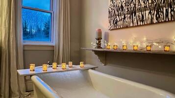Ein Badezimmer mit einer Badewanne, einem Fenster mit Vorhängen und einem Regal mit Kerzen.