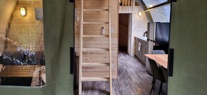A wooden interior with a staircase, a kitchen area, and a view through a window.