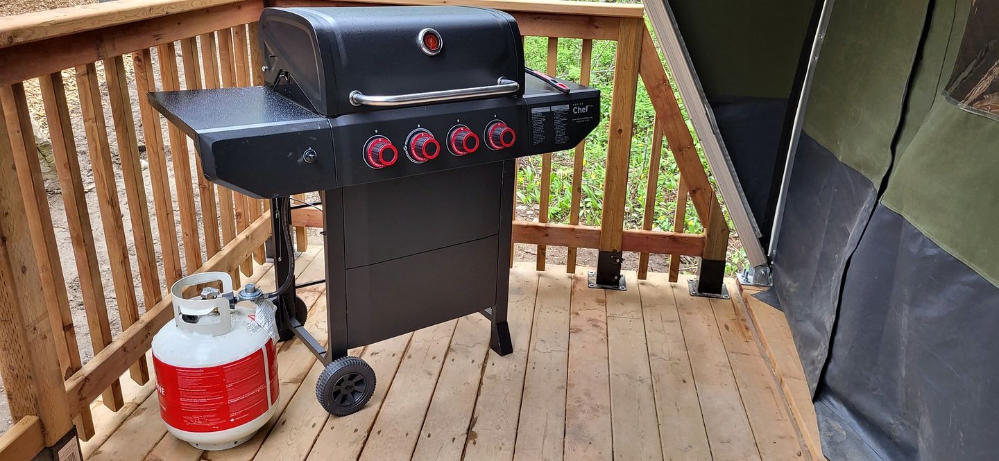 Un barbecue portatif doté de quatre brûleurs et d’une bouteille de gaz, installé sur une terrasse en bois.