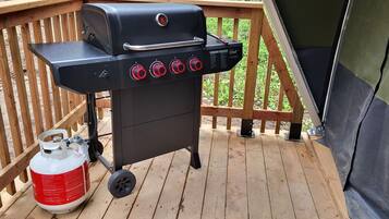 Un barbecue portatif doté de quatre brûleurs et d’une bouteille de gaz, installé sur une terrasse en bois.