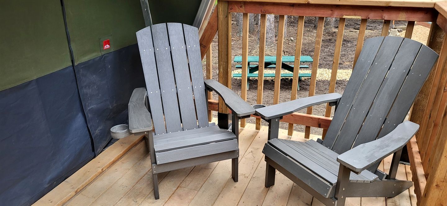 Two Adirondack chairs on a wooden deck with a green wall and a wooden railing in the background.