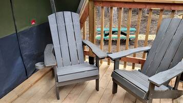 Deux fauteuils Adirondack sur une terrasse en bois, avec un mur vert et une balustrade en bois en arrière-plan.