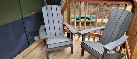Two Adirondack chairs on a wooden deck with a green wall and a wooden railing in the background.