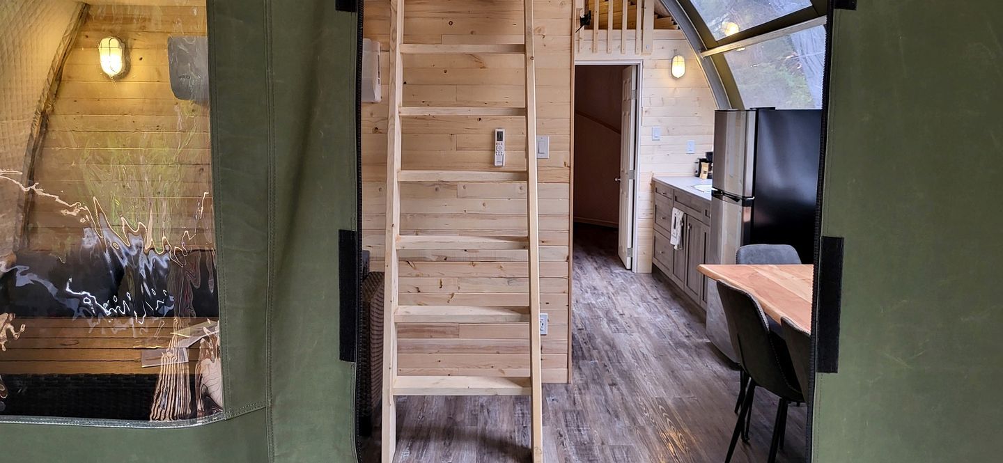 Un intérieur en bois avec un escalier, un coin cuisine et une vue par une fenêtre.
