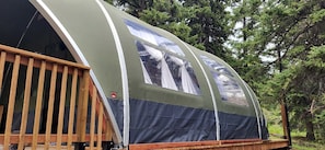 A large, semi-enclosed tent with a wooden deck, surrounded by trees. - Unique Tented Cabin Fully Furnished and Equipped Perfect for Groups or Families in Alberta (Beaver Mines)