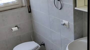 Et badeværelse med toilet, bidet og vask, flisemure og et vindue.