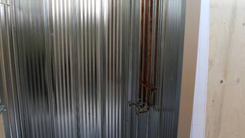 Une pièce aux murs métalliques, dotée d’un plancher en bois, d’une porte en métal et d’un tuyau vertical.