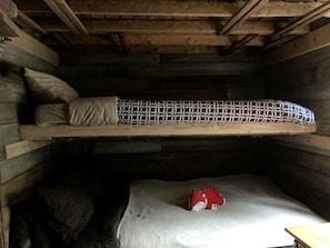 Un lit superposé avec un matelas et des oreillers, un jouet rouge sur le lit du bas et des murs en bois.
