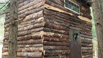 A rustic log cabin with a wooden door, a small window, and a porch.