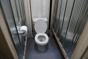 A small, narrow bathroom with a white toilet, a toilet paper holder, and a floor drain.