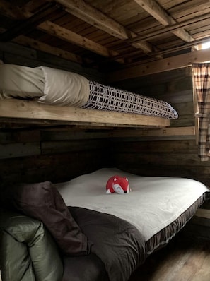 Un lit superposé avec un matelas et un oreiller sur le lit du haut, un oreiller sur le lit du bas et un jouet rouge sur le lit inférieur.