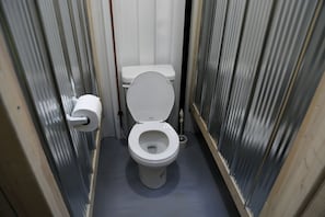Une petite salle de bain étroite, avec des toilettes blanches, un porte-rouleau de papier toilette et un drain au sol.