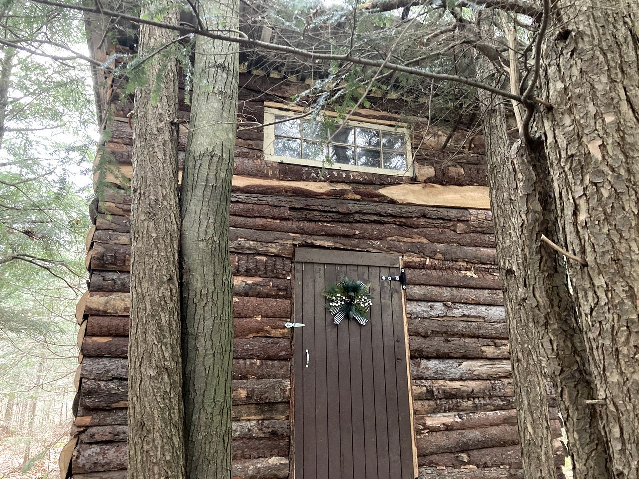 A rustic log cabin with a wooden door and a window above it.