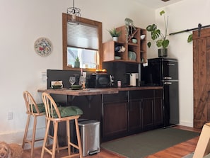A kitchen with a wooden island, bar stools, a trash can, a black refrigerator, and a window with blinds.