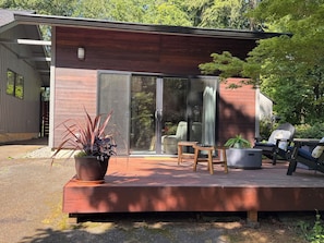 Une terrasse extĂ©rieure moderne, avec une table et des chaises en bois, une plante en pot et une porte-fenĂȘtre coulissante donnant sur un patio abritĂ©.