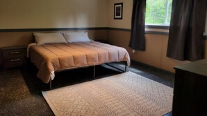 A bedroom with a bed, a nightstand, a dresser, a window with curtains, and a framed picture on the wall. - Group Cabin Lodge Surrounded by Nature with Beautiful Hiking Trails and Views in Alberta (Beaver mines)