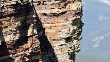 A rock formation with layered strata, a distant mountain, and a valley below.