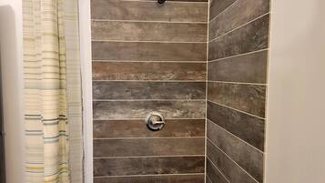 A shower with a striped curtain, a wall with horizontal tiles, and a metallic shower head.
