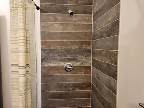 A shower with a striped curtain, a wall with horizontal tiles, and a metallic shower head.