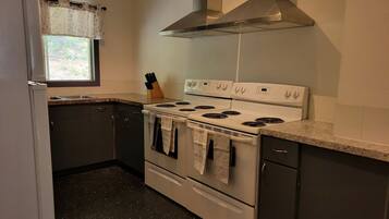 A kitchen with a stove, oven, and a window with a curtain.