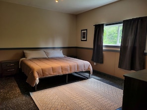 A bedroom with a bed, a nightstand, a dresser, a window with curtains, and a framed picture on the wall.