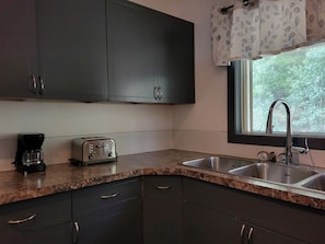 A kitchen with dark cabinets, a granite countertop, a toaster, a coffee maker, and a window with a view of trees.