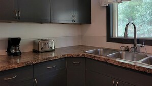 A kitchen with dark cabinets, a granite countertop, a toaster, a coffee maker, and a window with a view of trees. - Group Cabin Lodge Surrounded by Nature with Beautiful Hiking Trails and Views in Alberta (Beaver mines)