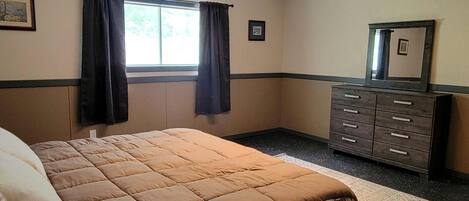 Un dormitorio con cama, cómoda, ventana con cortinas y una alfombra pequeña.