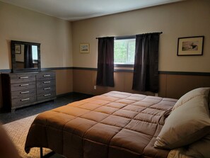 A bedroom with a bed, dresser, window with curtains, and a framed picture on the wall.