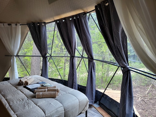 A tent-style bedroom with a bed, towels, and a view of greenery outside.