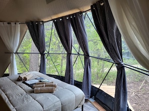A tent-style bedroom with a bed, towels, and a view of greenery outside. - Family-Friendly Dome Perfect for a Cozy and Tranquil Escape in Alberta (Beaver Mines)