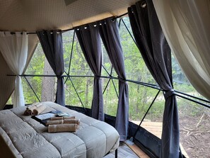 A tent-style bedroom with a bed, towels, and a view of greenery outside.