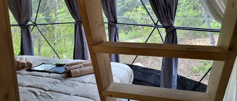 A bedroom with a bed, a wooden ladder, and a window with curtains.