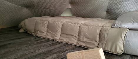 Una cama con colchón acolchado y almohadas, suelo de madera y cabecero de madera.