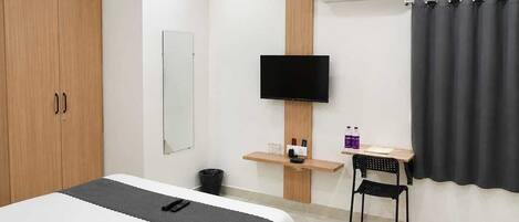 A hotel room with a bed, a desk, a chair, a TV, an air conditioning unit, and a wardrobe.