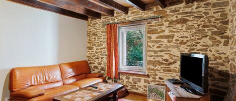 A cozy living room with a leather sofa, a wooden coffee table, a television on a wooden stand, and a stone wall.