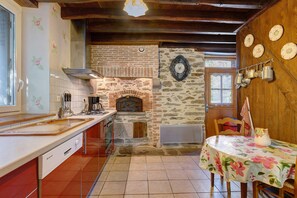 A kitchen with a stone fireplace, a wooden ceiling, and a dining area with a floral tablecloth.