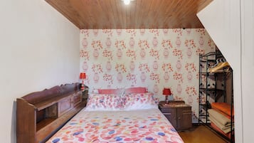 A bedroom with a wooden ceiling, a bed with floral bedding, a nightstand with a lamp, and a wardrobe.