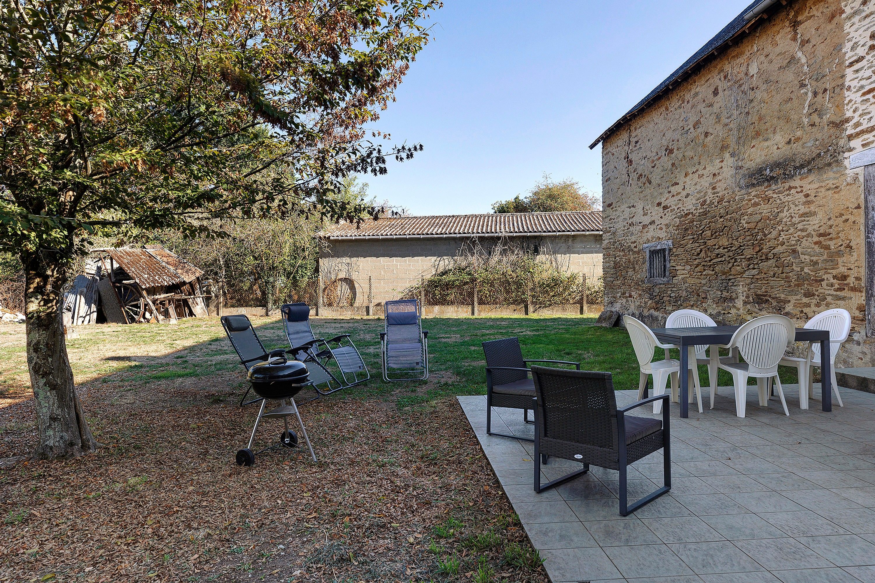 Une terrasse extérieure avec une table et des chaises, un barbecue et un bâtiment en pierre en arrière-plan.
