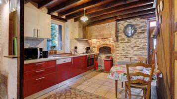 Una cocina con armarios rojos, pared de piedra, chimenea de ladrillo y un comedor con mesa y sillas.