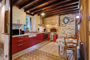 A kitchen with red cabinets, a stone wall, a brick fireplace, and a dining area with a table and chairs.