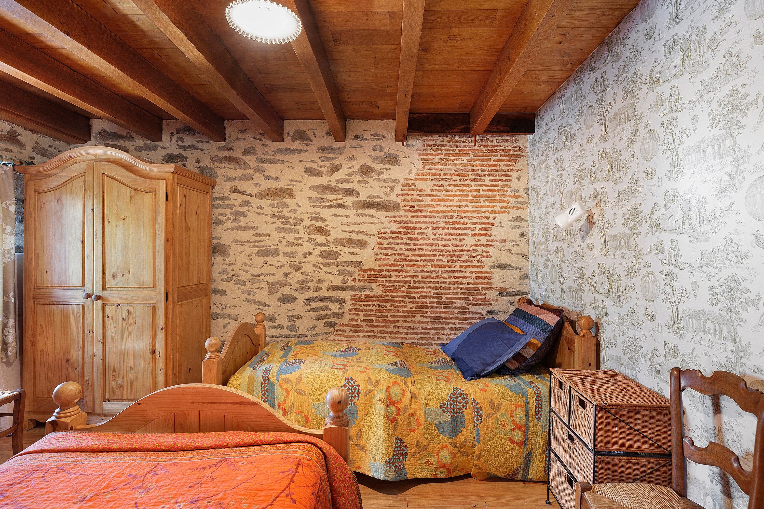 A bedroom with a wooden bed, a wooden wardrobe, a stone wall, and a patterned wallpaper.