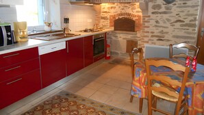 A kitchen with red cabinets, a stone wall, a brick fireplace, and a dining area with a table and chairs. - Holiday Home “La Charmille” with Private Terrace and Garden (Nouzerolles)