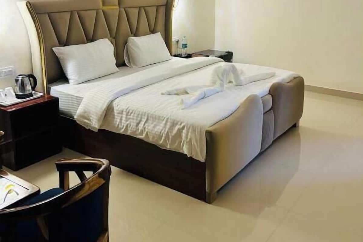 Una cama bien hecha con cabecera, una mesita de noche con lámpara y una silla en una habitación limpia y bien iluminada.