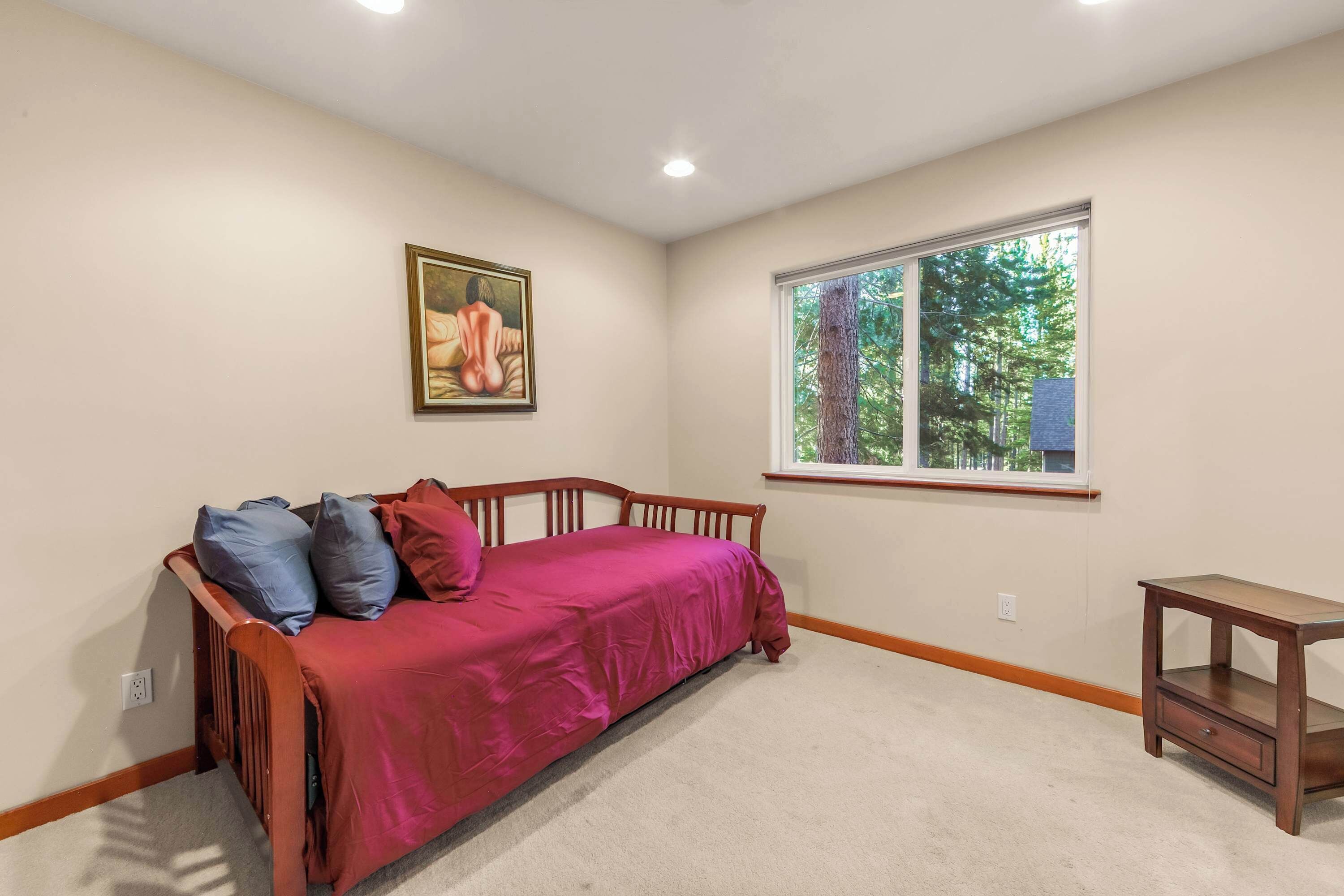 A bedroom with a bed, a window, a painting, and a small table.