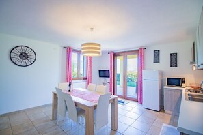 Ein Essbereich mit Tisch, Stühlen, einer Uhr, einem Fernseher und einer Küchenzeile inklusive Kühlschrank und Mikrowelle.