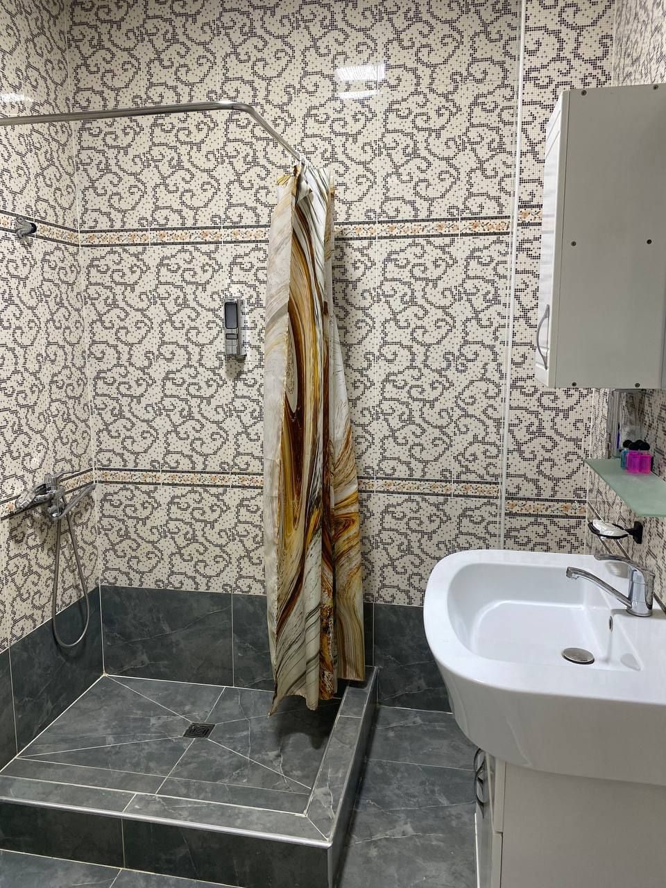 Ein Badezimmer mit gemusterten Fliesen, einer Dusche, einem Waschbecken und einem Spiegel.