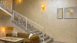 A staircase with ornate metal railings, a sofa, a coffee table, and two wall-mounted lamps. - Sumaya Hotel (Tashkent)