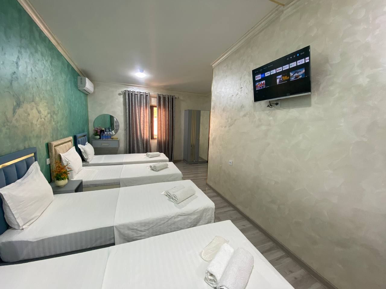 A hotel room with three beds, a television mounted on the wall, and a window with curtains.