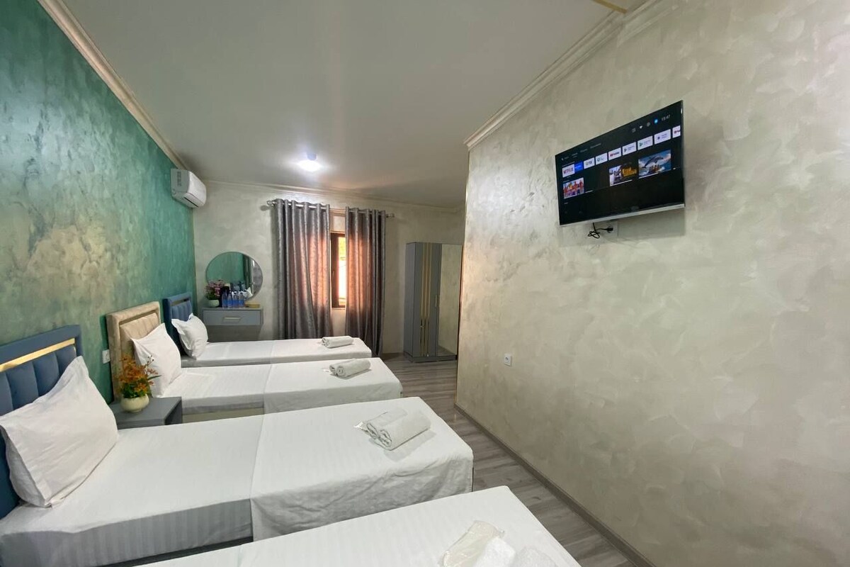 A hotel room with three beds, a television mounted on the wall, and a window with curtains.